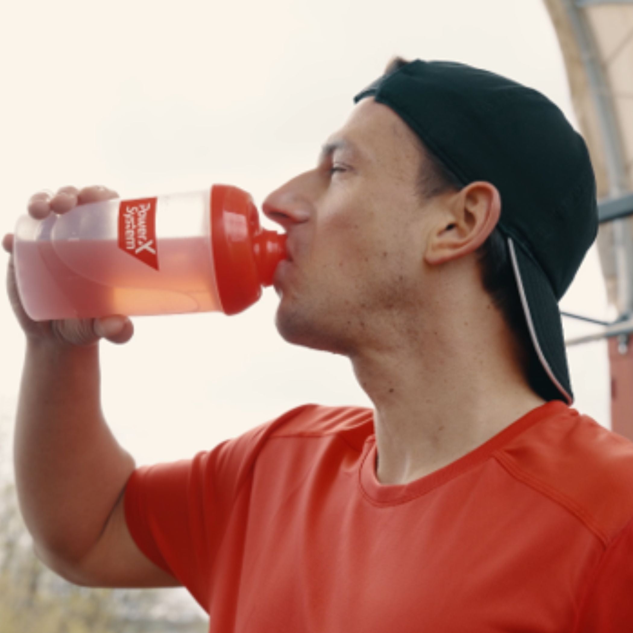 Mann trinkt aus einem Shaker eine Protein Limo. Die Packungen der beiden Sorten im Vordergrund.